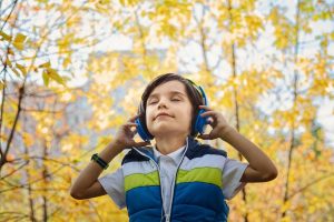 Little boy wearing headphone listening to music outside in the fall season -Total Vision and Hearing in Ancaster, Ontario