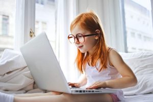 Little girl wearing eyeglasses browsing on laptop - Total Vision and Hearing in Ancaster, Ontario